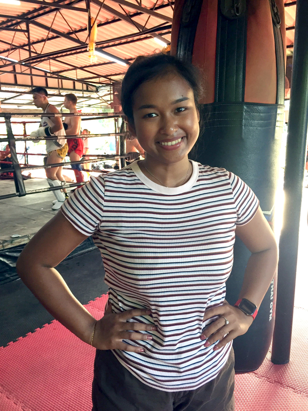Die Sportstudio-Managerin Polla Konputon steht vor einem Boxring, in dem gerade Muay Thai trainiert wird. 