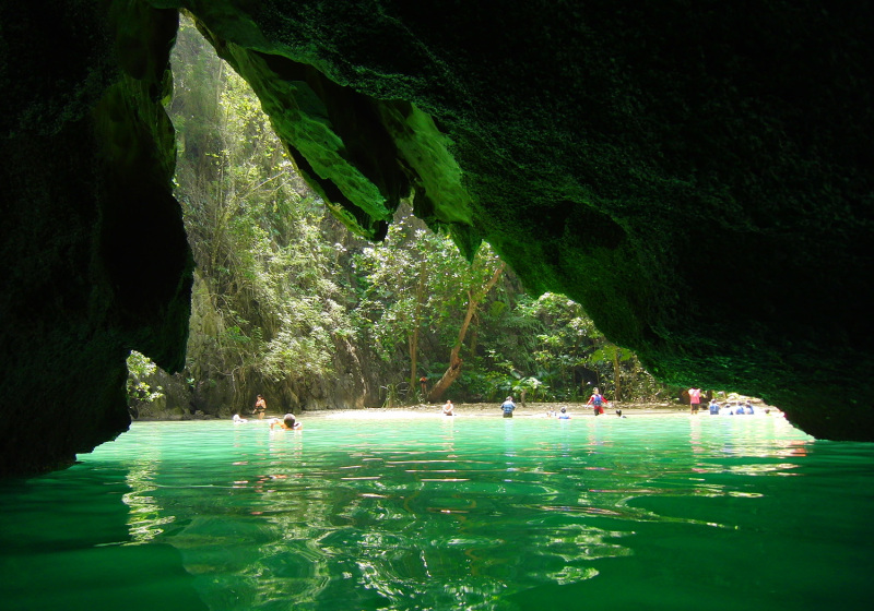 Blick aus der Fledermaushöhle auf das grün schimmernde Lagunenwasser und den weißen Strand.