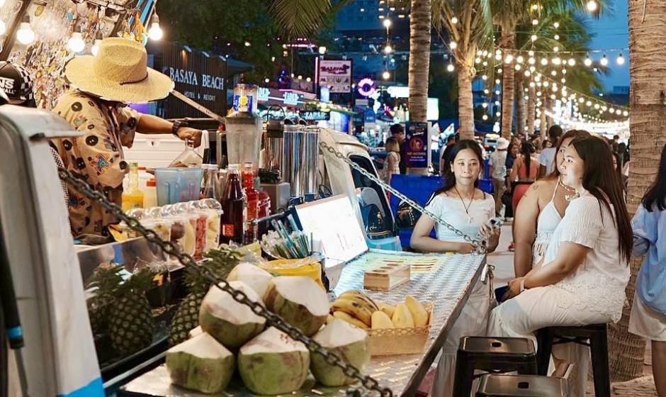 Besucher sitzen an einem Straßenstand mit frischen Getränken und Snacks entlang der festlich beleuchteten Strandpromenade. Bild: PR Pattaya