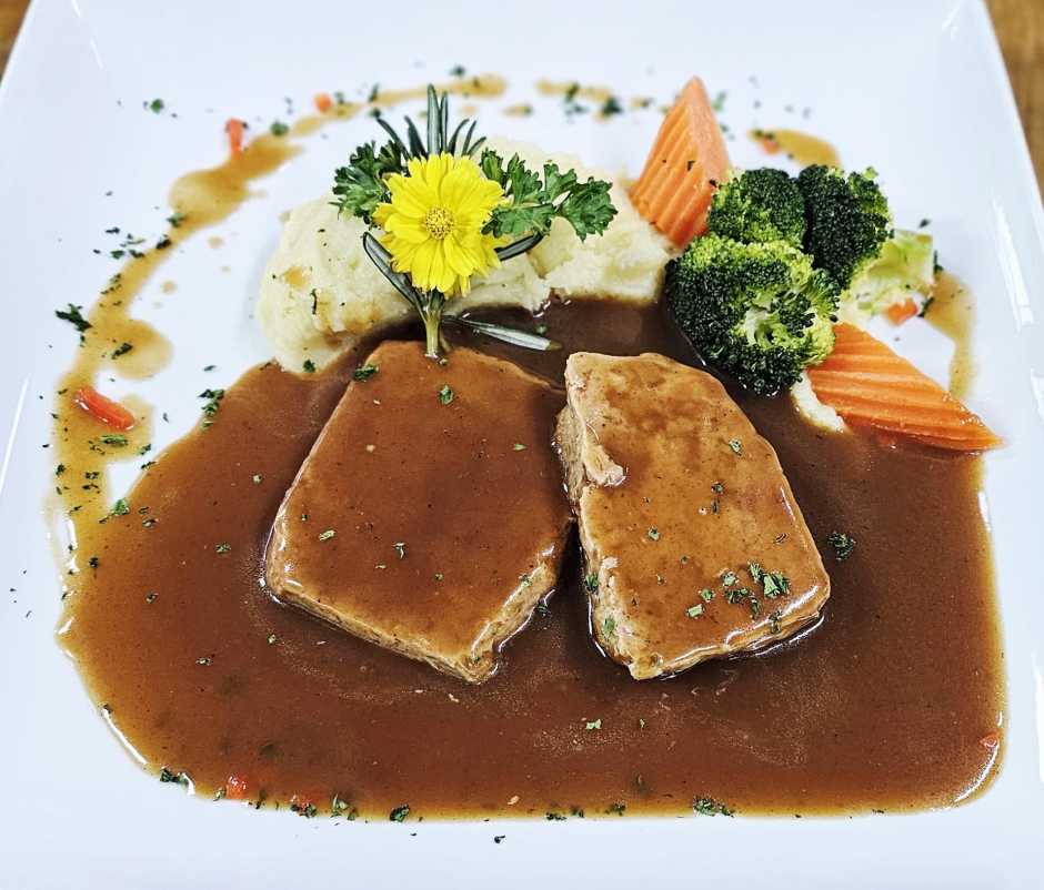 Hausgemachter Hackbraten mit kräftiger Bratensauce, serviert mit Kartoffelstock und Gemüse.