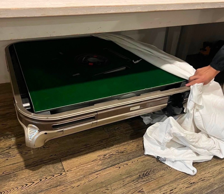 Die Einsatzkräfte entdecken einen unter einem Tisch verborgenen automatischen Spieltisch im mutmaßlichen Casino des Hotels. Bild: Central Investigation Bureau (CIB)