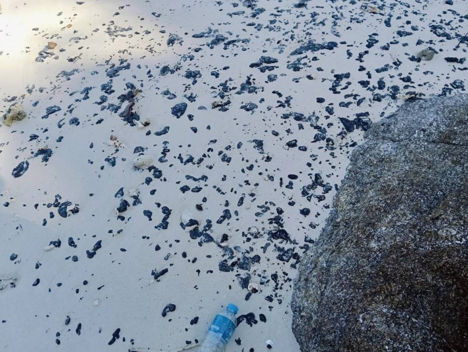 Schwarze Teerklumpen liegen verstreut auf einem Strand von Koh Racha, nachdem Öl aus dem gesunkenen Schiff ausgetreten war. Bild: Department of Marine and Coastal Resources (DMCR)