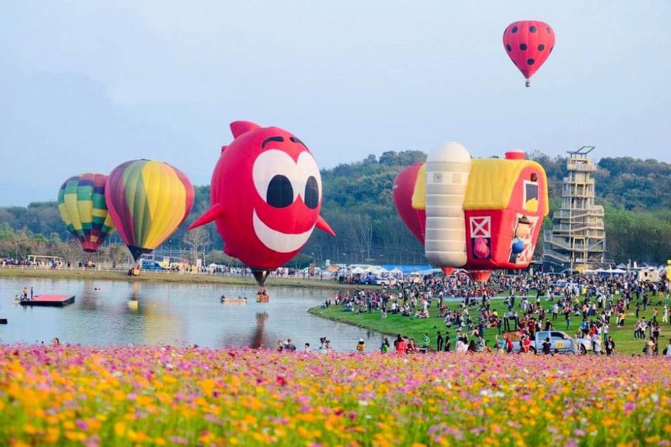 Sonderformen-Heißluftballons steigen über dem See auf, während Besucher das Geschehen vom Ufer aus verfolgen. Foto: Singha Park Chiang Rai