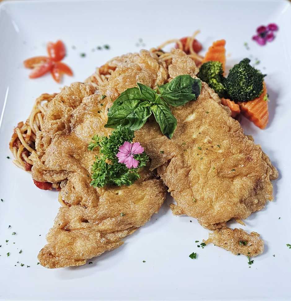 Zartes Chicken Piccata auf Spaghetti in Tomatensauce, serviert mit frischem Gemüse.