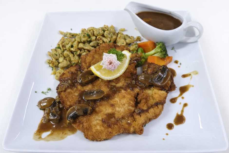 Knuspriges Poulet-Schnitzel mit Jägersauce, Fettuccine und Buttergemüse wird im Rahmen der Wochenkarte serviert.