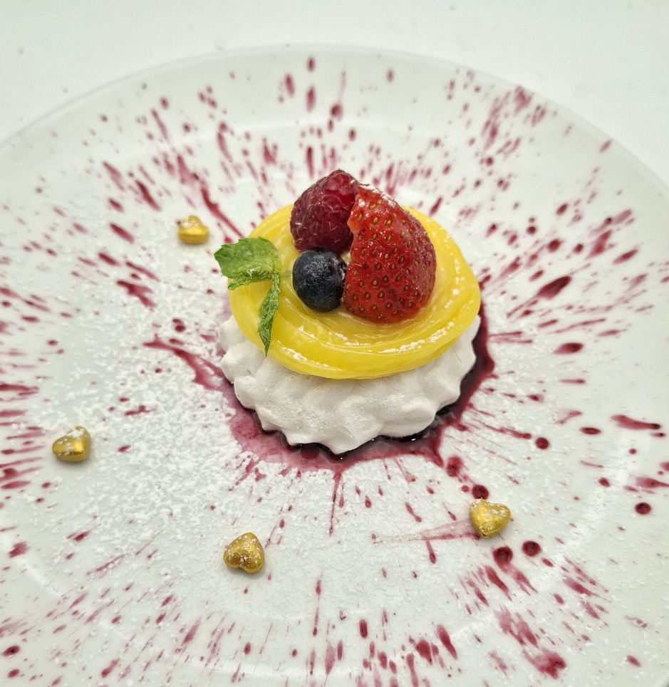 Lemon Curd Pavlova mit frischen Beeren auf Baiserboden und fruchtiger Sauce angerichtet.