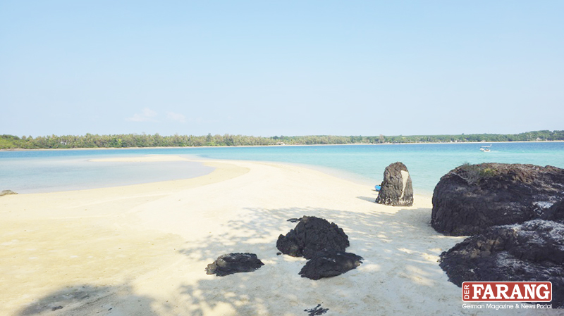 Eine schmale Sandbank vor Koh Kham zieht sich durch türkisblaues, flaches Wasser, gesäumt von dunklem Vulkangestein und feinem Sand. 