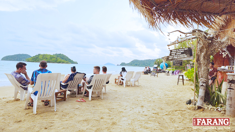 Urlauber sitzen in der tropischen Baan Yai Beach Bar am Ao Kratueng im Sand und schauen hinaus auf das Meer.