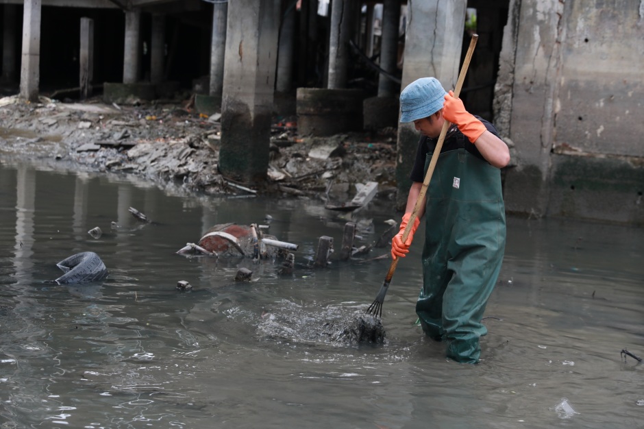 Ein Mitarbeiter entfernt Schlamm und Abfälle aus dem Wasserbereich unter der Brücke am Naklua-Kanal. Bild: TMN.TV
