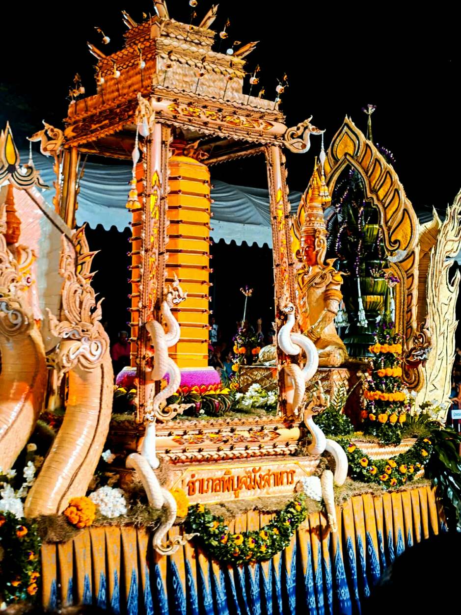 Ein festlich geschmückter Kerzenwagen wird während der abendlichen Präsentationen rund um Thung Si Mueang in Szene gesetzt.