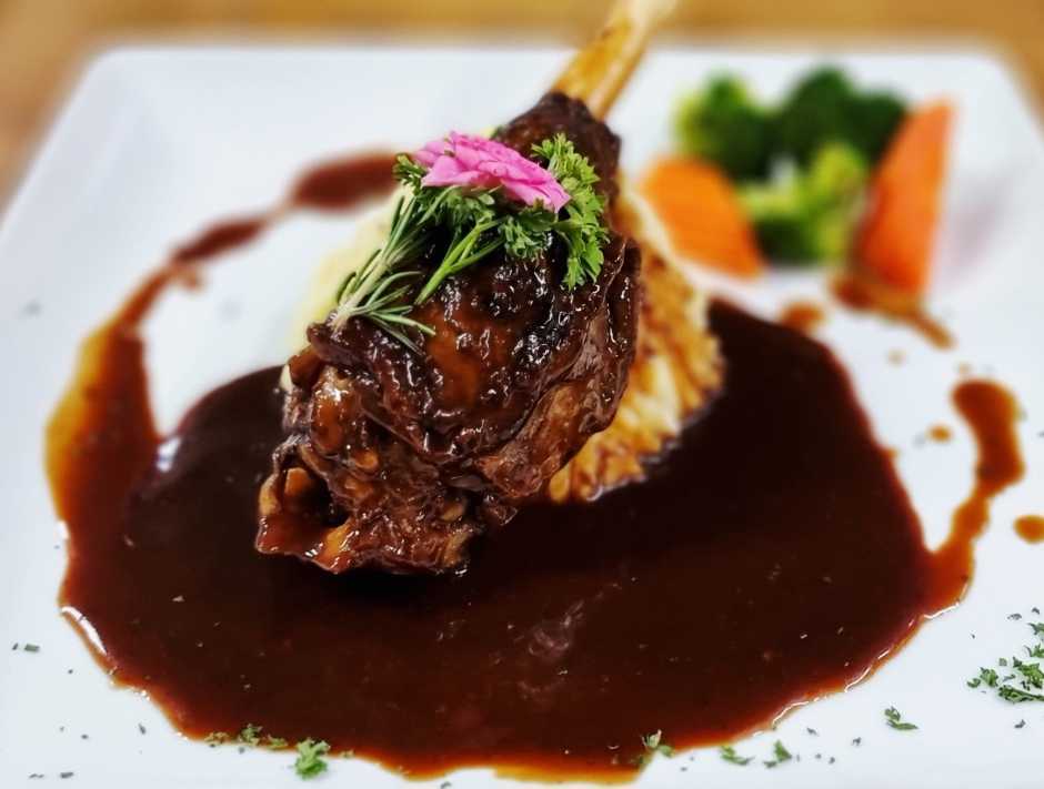 Die langsam geschmorte australische Lammhaxe wird mit Kartoffelpüree, Gemüse und kräftiger Jus serviert.
