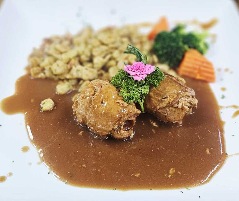 Geschmorte Schweineroulade mit Speck-, Zwiebel- und Gewürzgurkenfüllung, dazu Spätzli und Gemüse.