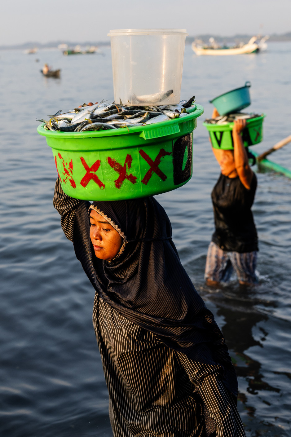 Alltag am Meer: Eine Frau  trägt frischen Fang an Land. Foto: picture alliance / NurPhoto | Garry Lotulung